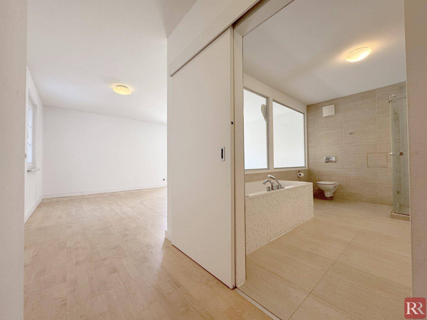 Schlafzimmer mit Holzboden und Schiebetür, die zum modernen Badezimmer führt.