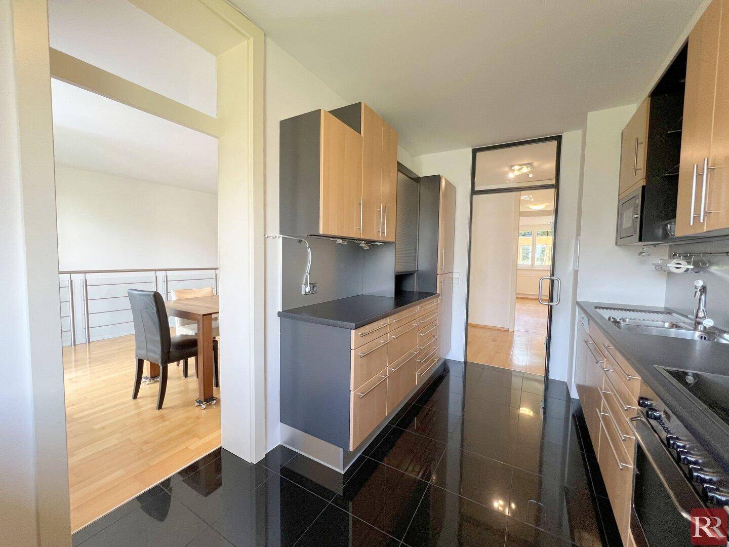 Funktionale Küche mit schwarzen Fliesen, modernen Holz- und Grauschränken und Blick zum Essbereich.