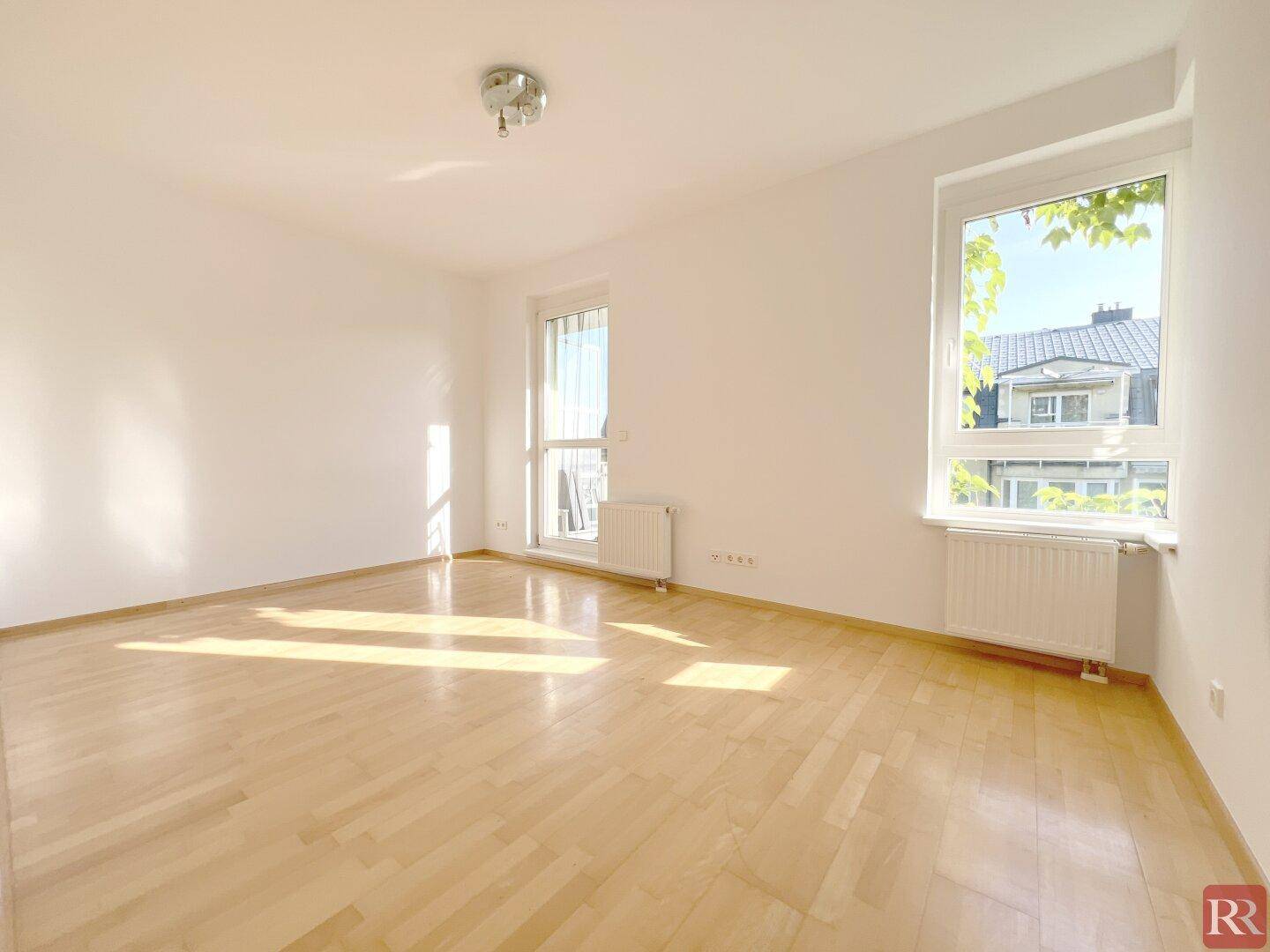 Helles Zimmer mit Parkettboden, großen Fenstern und Zugang zu einem französischen Balkon.