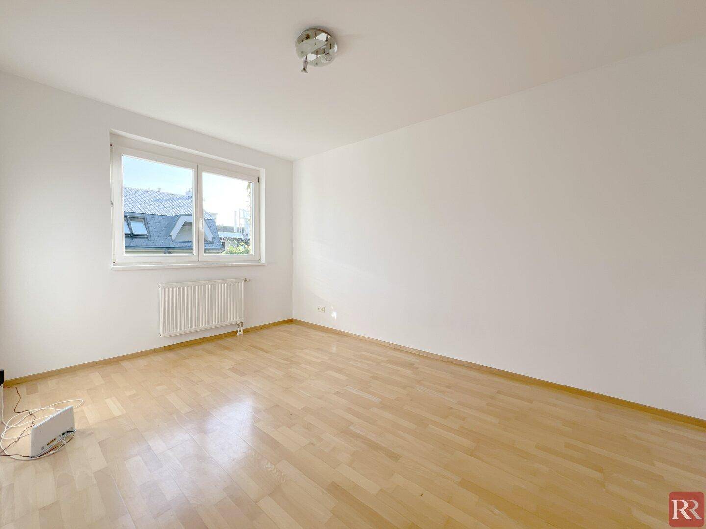 Freundliches Zimmer mit Parkettboden und großem Fenster, das viel Tageslicht hereinlässt.