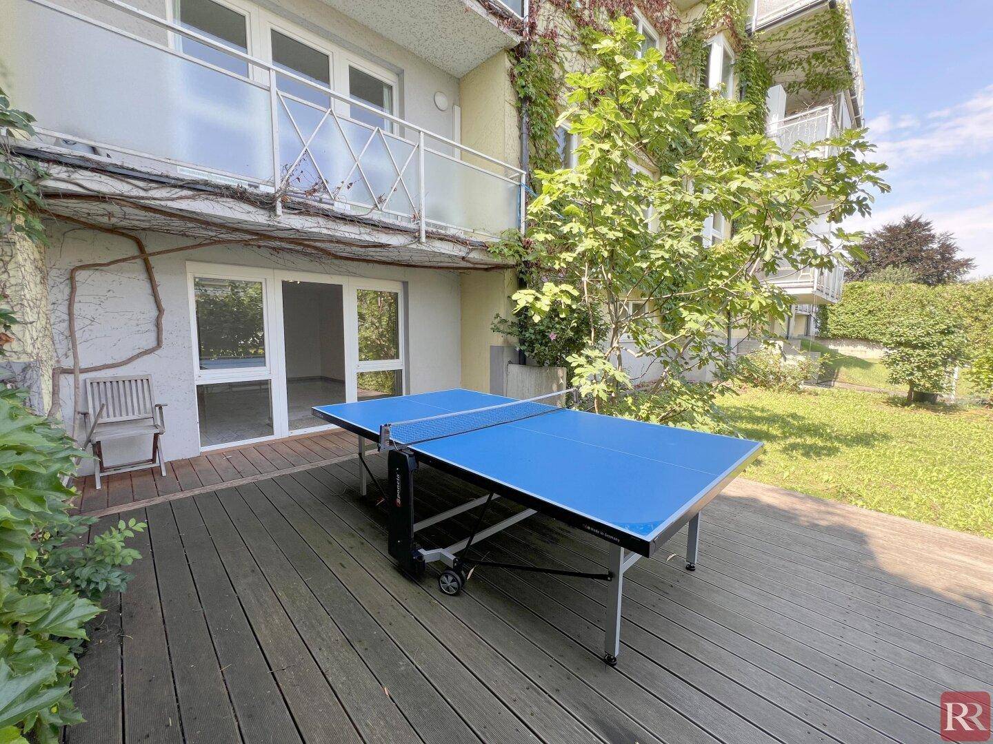 Große Holzterrasse mit Tischtennisplatte und direktem Zugang zum Gebäude.