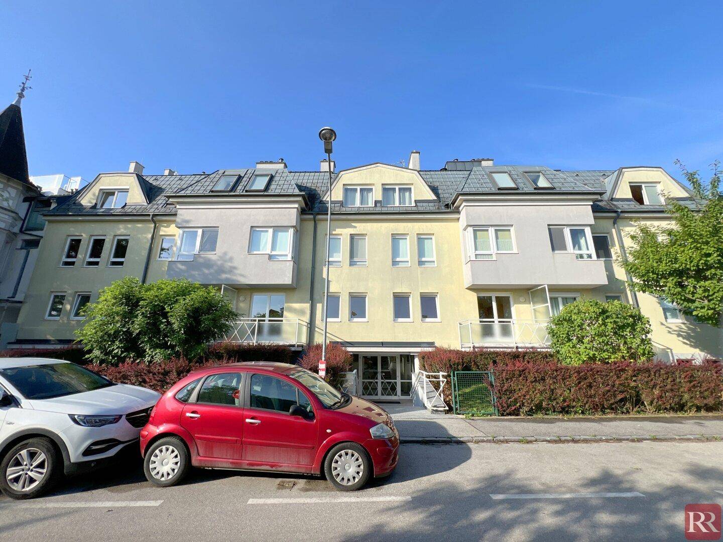 Außenansicht eines Mehrfamilienhauses mit gepflegter Fassade und Parkplätzen davor.