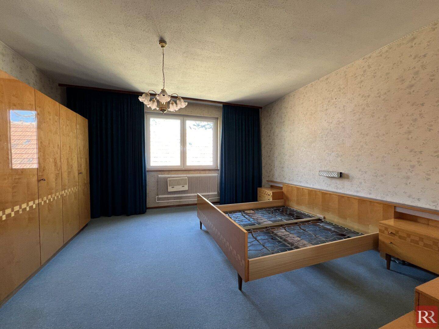 Schlafzimmer mit Doppelbettrahmen, großem Kleiderschrank und blauem Teppichboden.