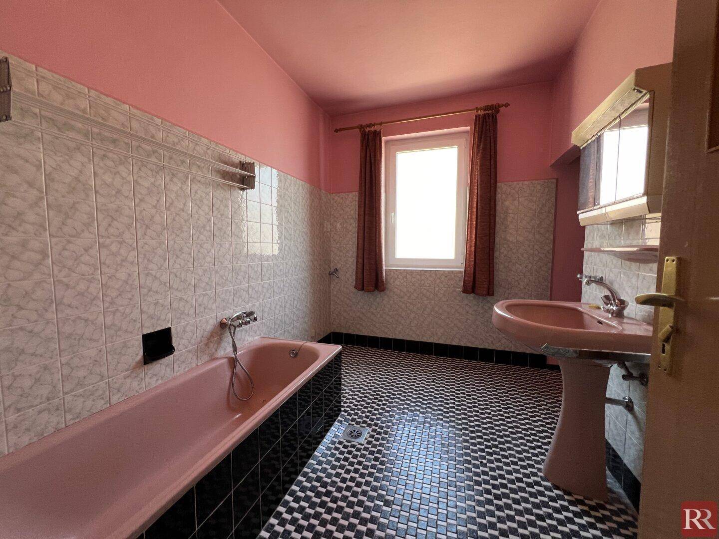 Badezimmer im 80er-Jahre-Stil mit rosa Badewanne, Waschbecken und schwarz-weißem Mosaikboden.