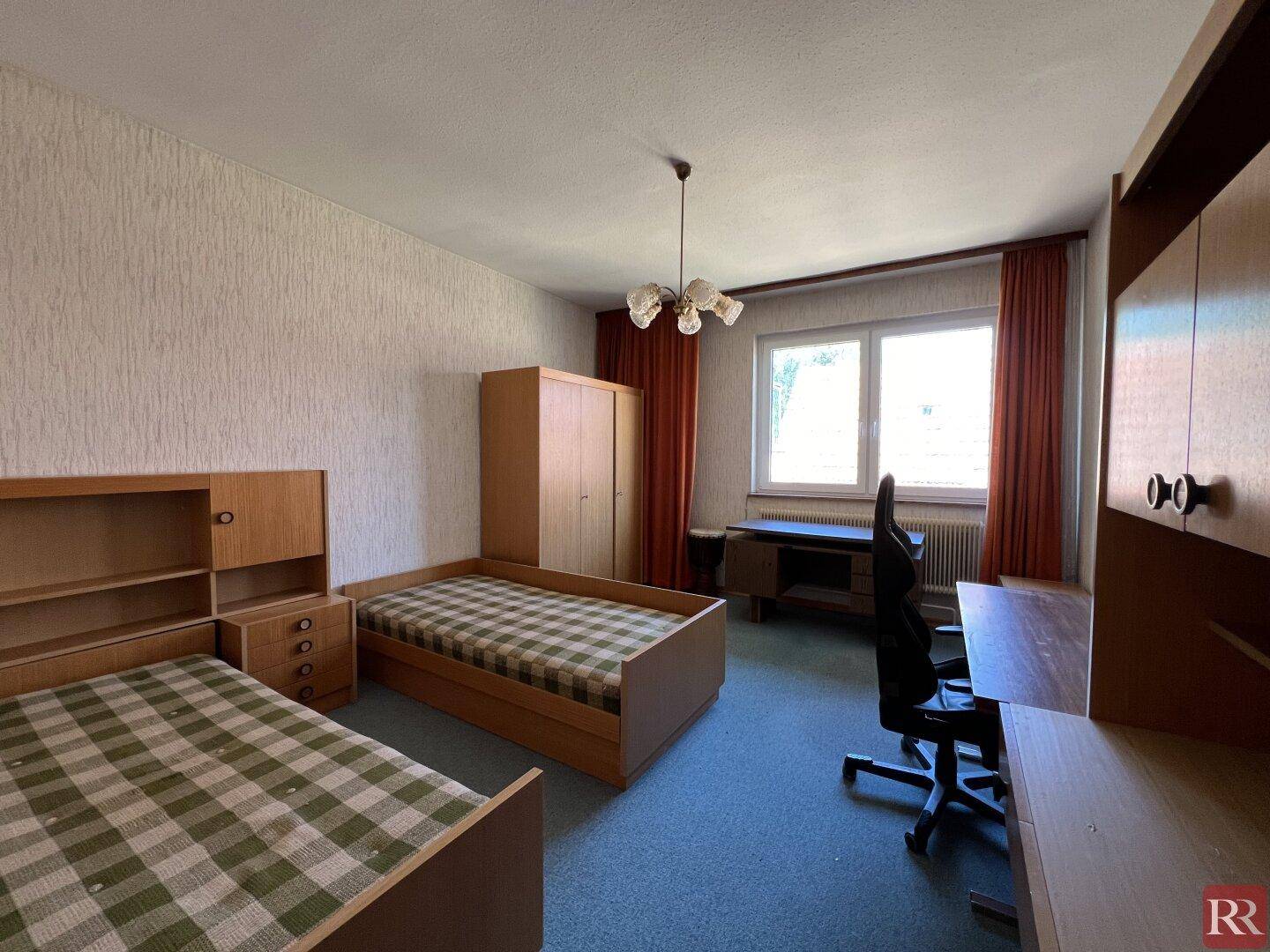 Kinder- oder Gästezimmer mit zwei Einzelbetten, Schreibtisch und blauem Teppichboden.
