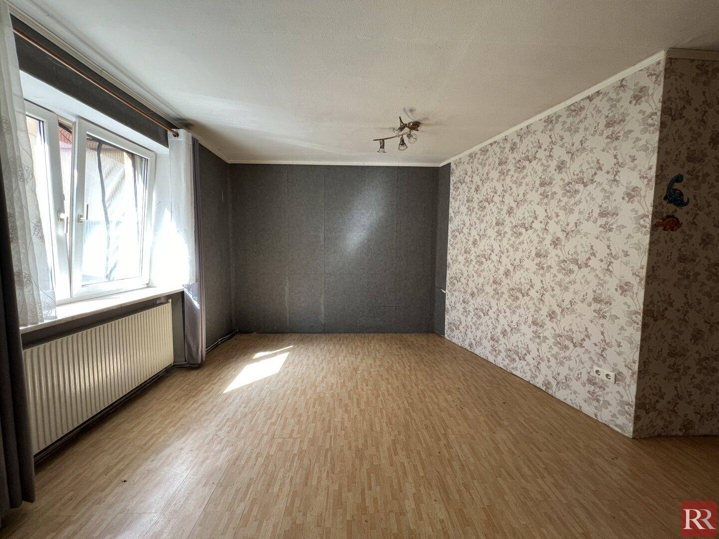 Leerer Raum mit Laminatboden, einer gemusterten Tapetenwand und einem großen Fenster.