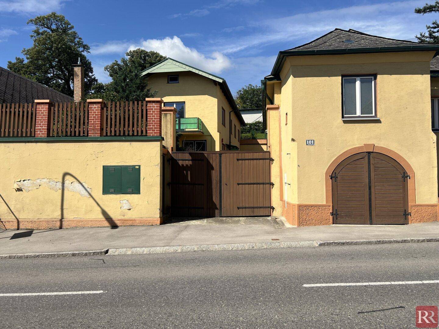 Zwei gelbe Gebäude von der Straße aus gesehen, eines mit einem großen Holztor und Bogen.