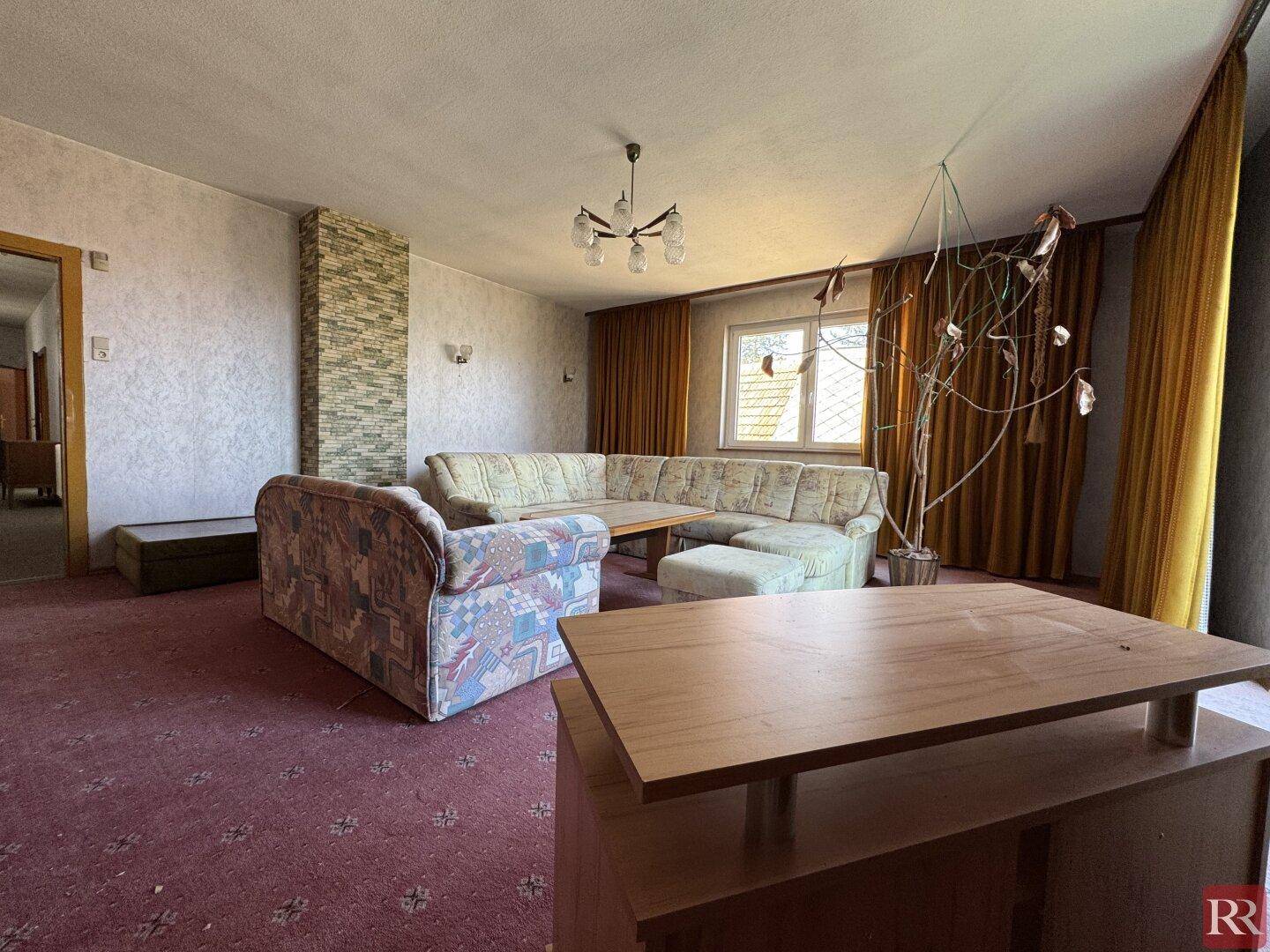 Wohnzimmer mit gemütlicher Sitzecke, Teppichboden und einer Wand mit Steinverkleidung.
