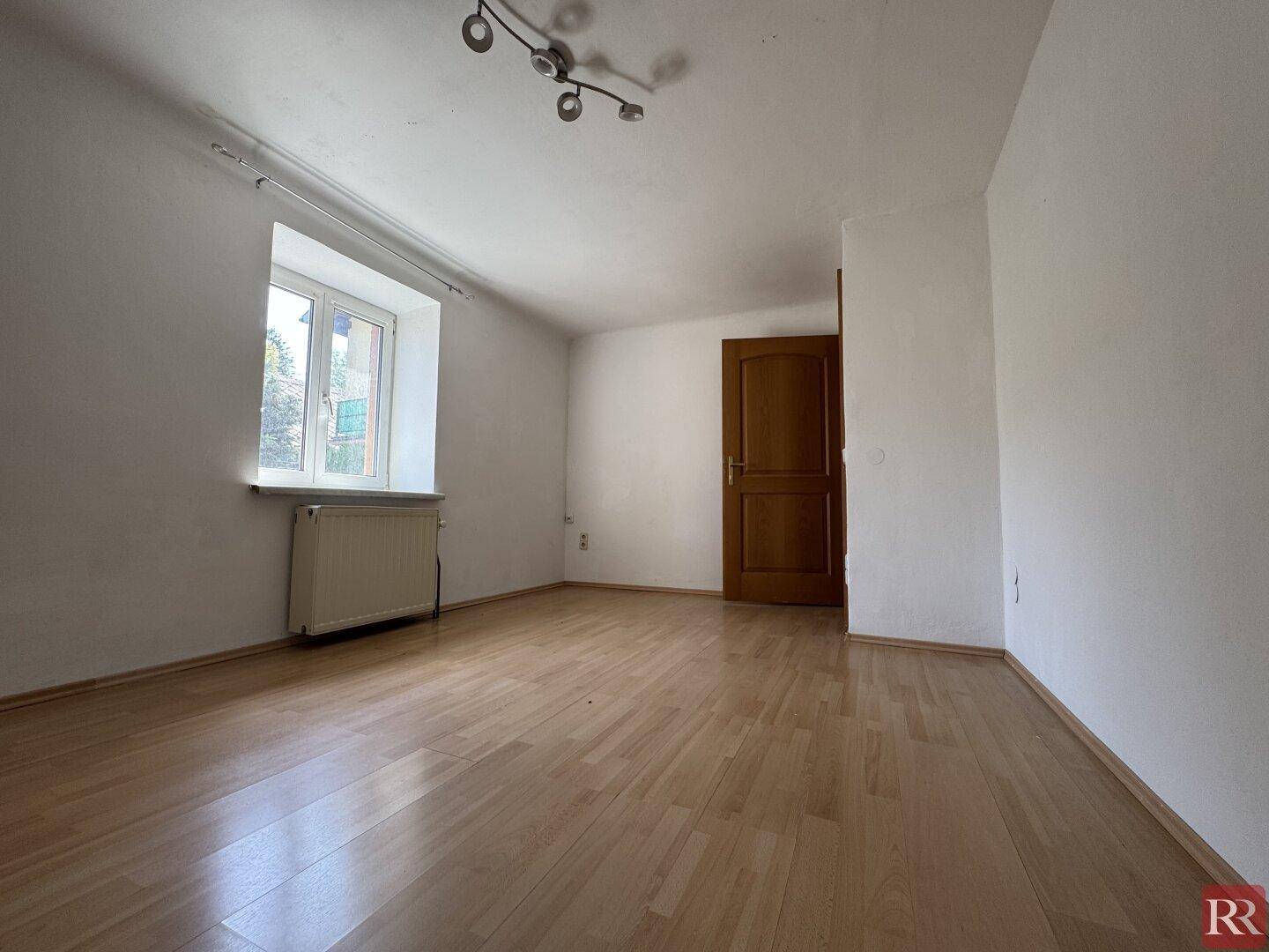 Heller, leerer Raum mit Laminatboden, weißen Wänden und einer Holztür.
