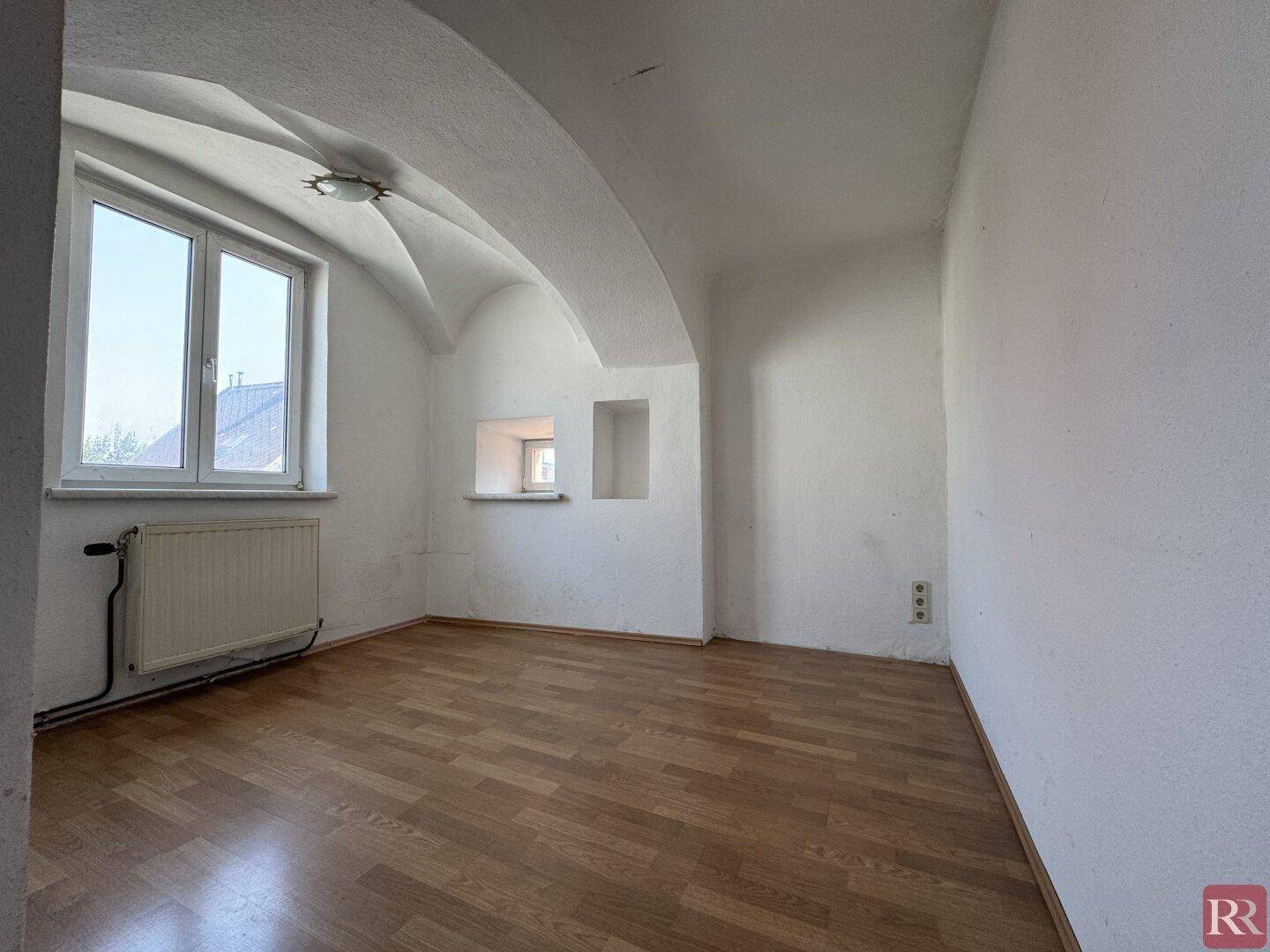 Leerer Raum mit beeindruckender Gewölbedecke, Laminatboden und einem großen Fenster.