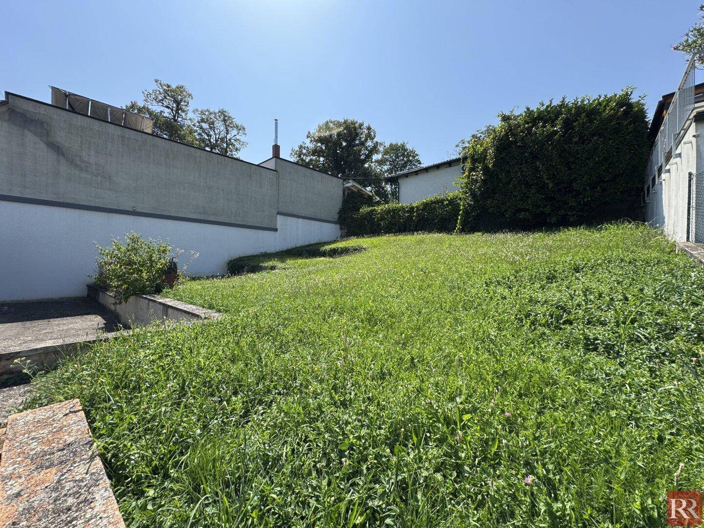 Weitläufiger, unebener Gartenbereich mit üppigem Grün und sonnigem Wetter.