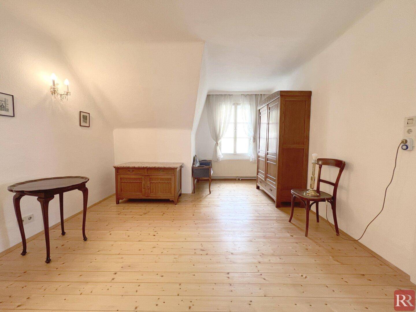 Helles Dachzimmer mit Holzboden, Dachschräge und traditionellen Holzmöbeln.