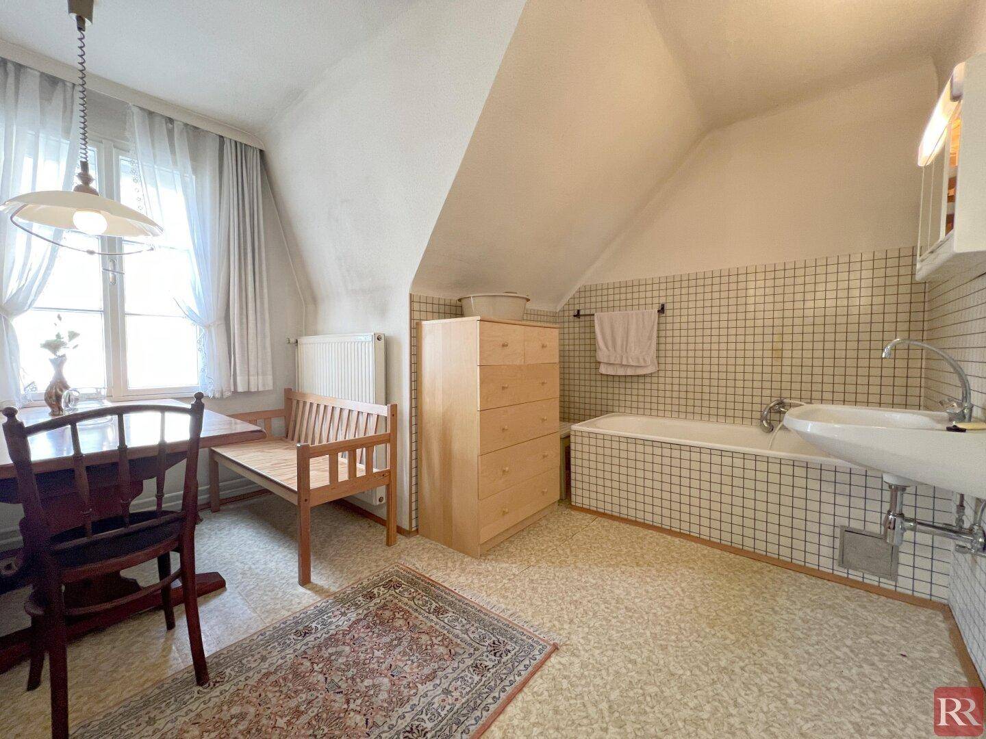 Dachgeschoss-Badezimmer mit Badewanne, Waschbecken und Essbereich, unter Dachschräge.