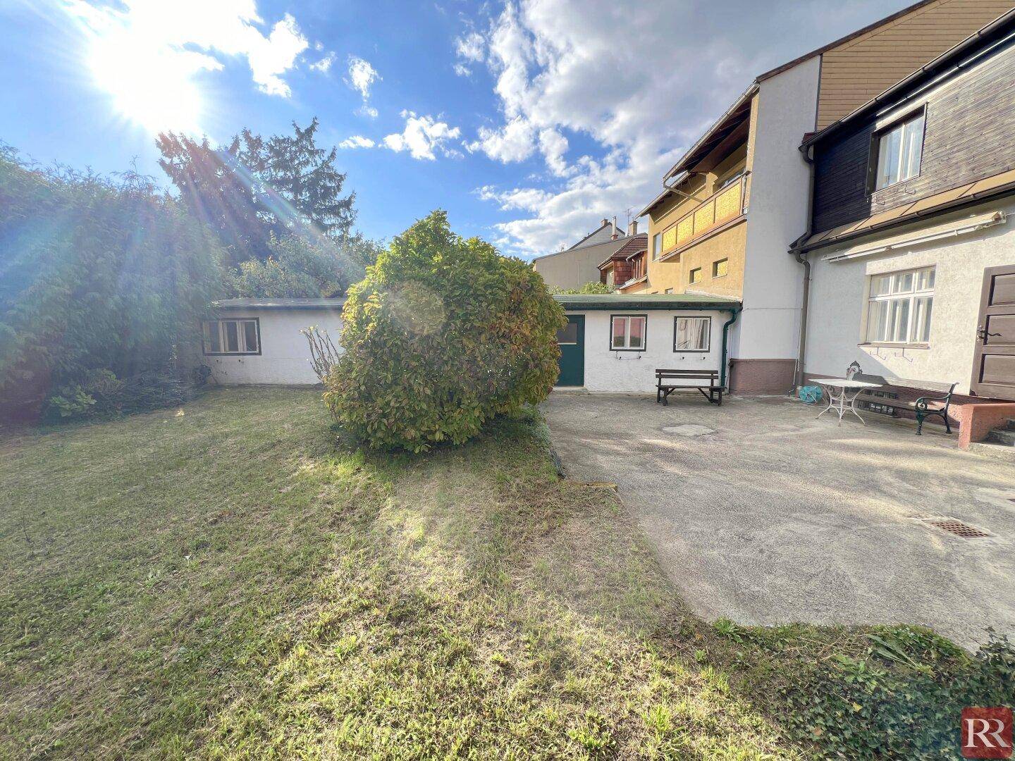 Gepflegter Garten mit Rasenfläche und Sitzbereich, umgeben von üppigem Grün.