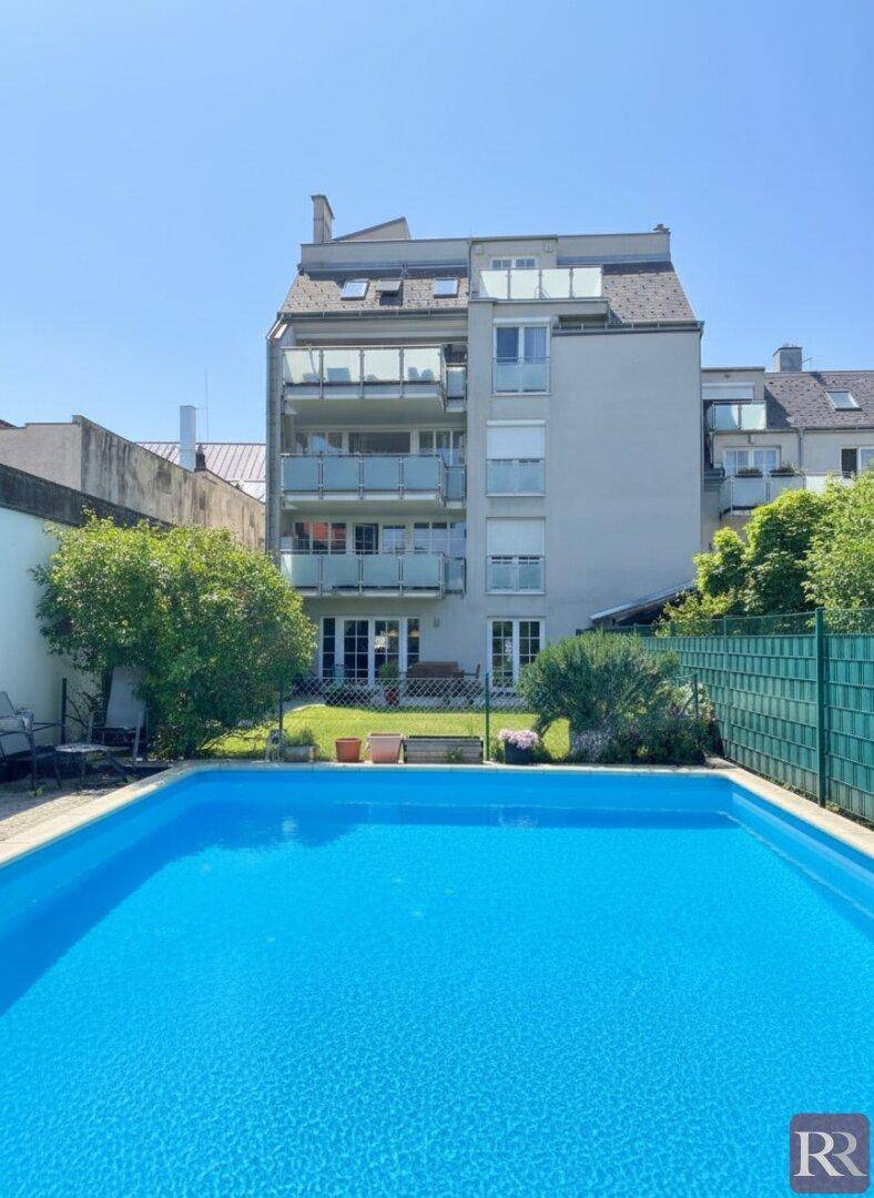Außenansicht des Gebäudes mit einem großen, blauen Swimmingpool im Vordergrund.