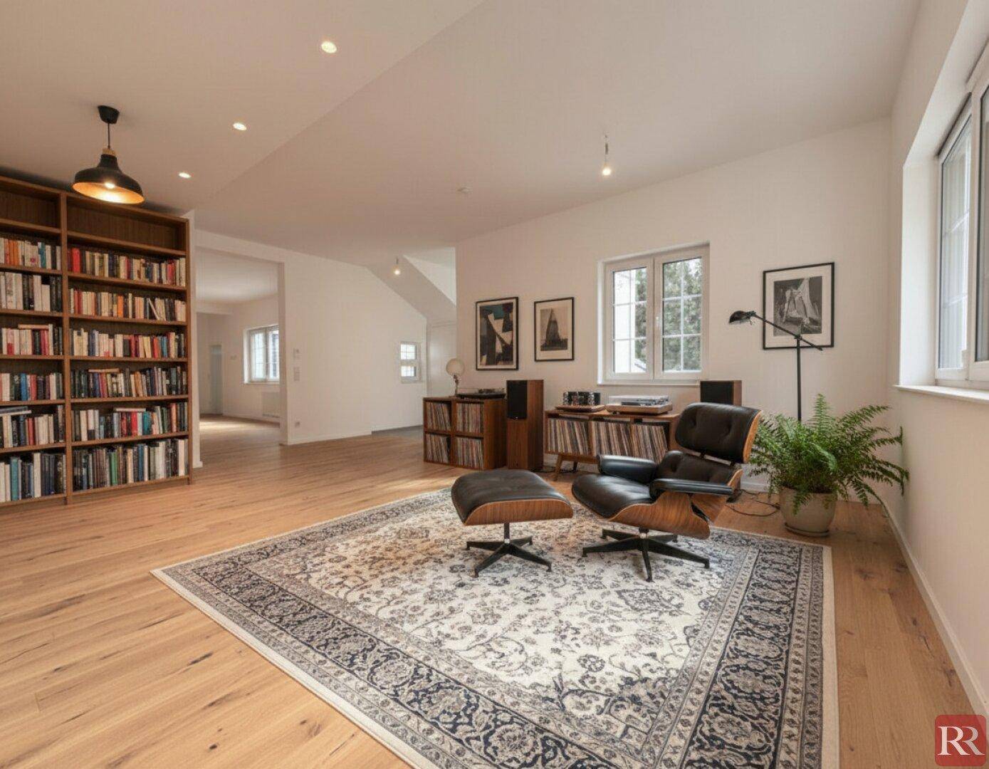Gemütlicher Wohnbereich mit Lesesessel, großem Bücherregal und Holzboden.