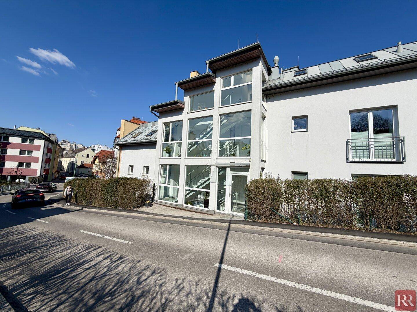 Moderne Gebäudefassade mit großer Glasfront und einem französischen Balkon an einem sonnigen Tag.