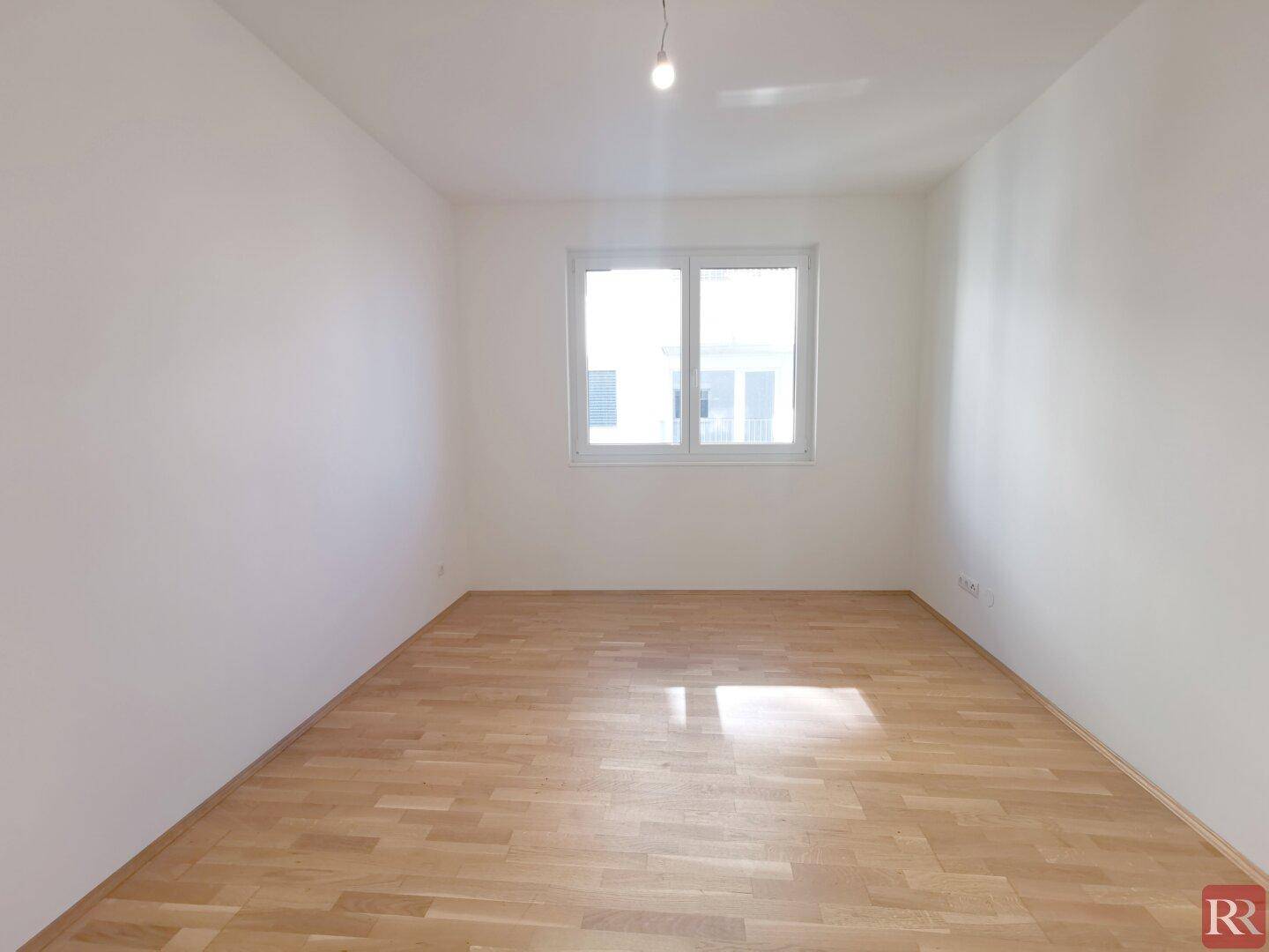 Leeres Zimmer mit hellem Parkettboden und großem Fenster, bereit zur individuellen Gestaltung.