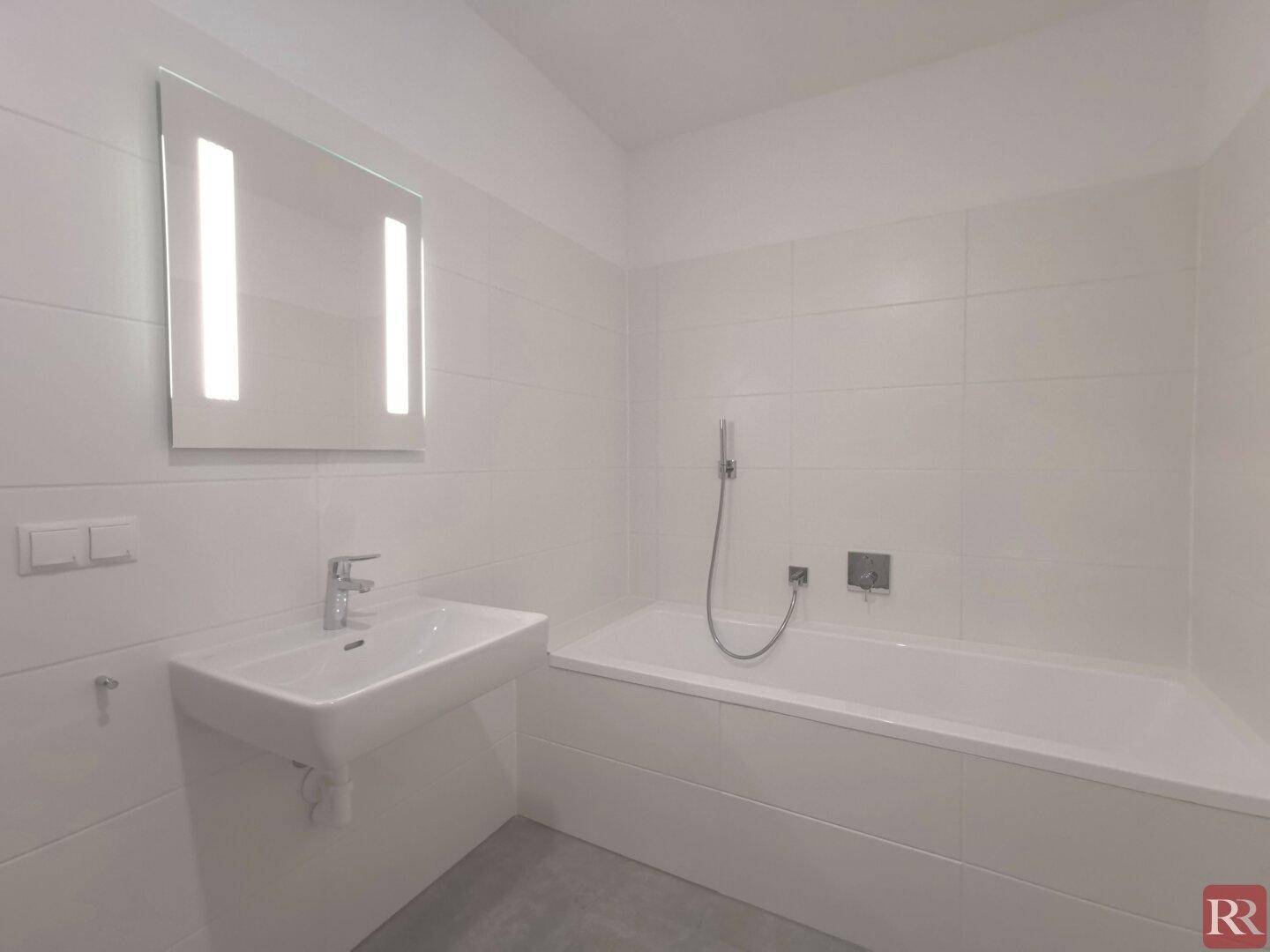 Modernes Badezimmer mit Badewanne, Wandwaschbecken und großen weißen Fliesen.