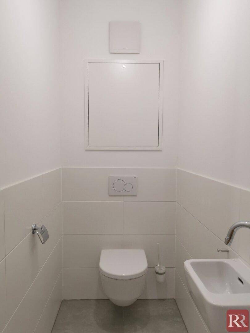 Separates Gäste-WC mit Wand-WC, kleinem Waschbecken und weißen Wandfliesen.