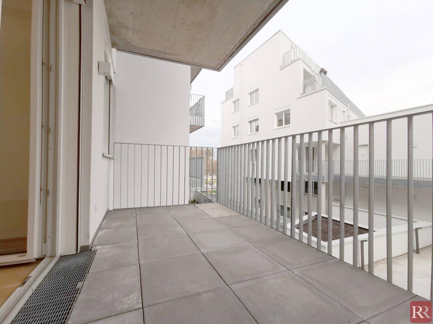 Geräumiger Balkon mit Fliesenboden und Blick auf die umliegenden Neubauten.