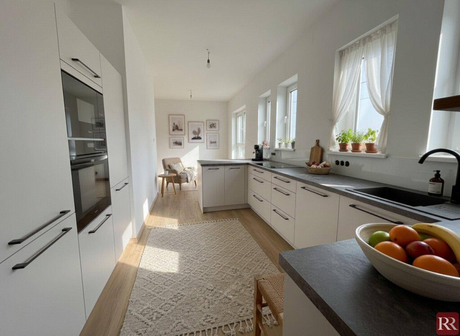 Moderne Küche mit weißen Schränken, dunklen Arbeitsplatten und viel Tageslicht.