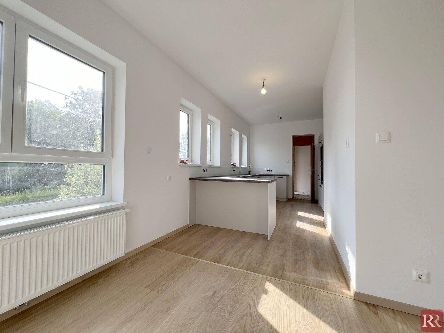 Helle, leere Küche mit Kücheninsel, großen Fenstern und Holzboden.