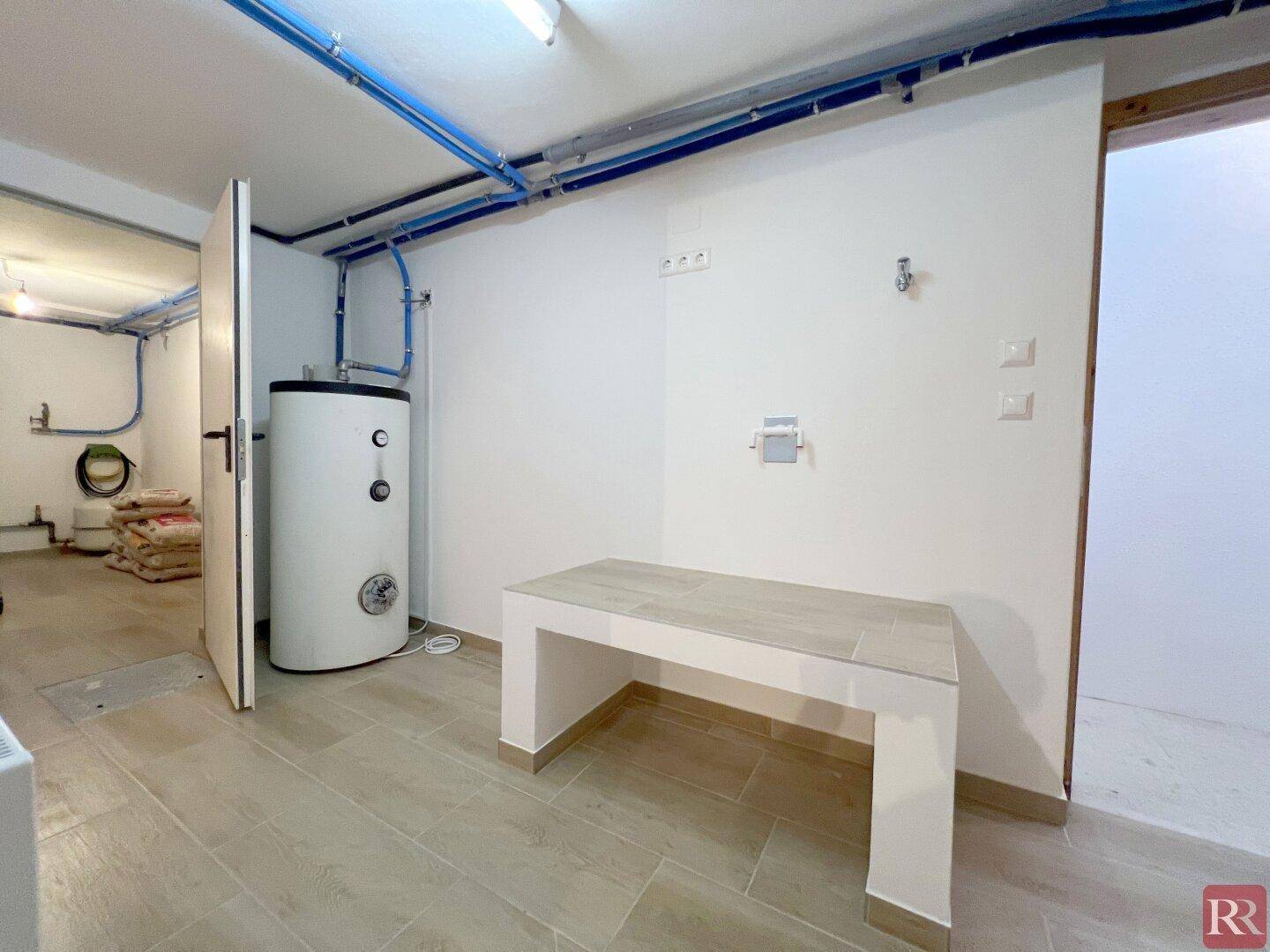 Hauswirtschaftsraum im Keller mit Warmwasserspeicher und sichtbaren Leitungen.