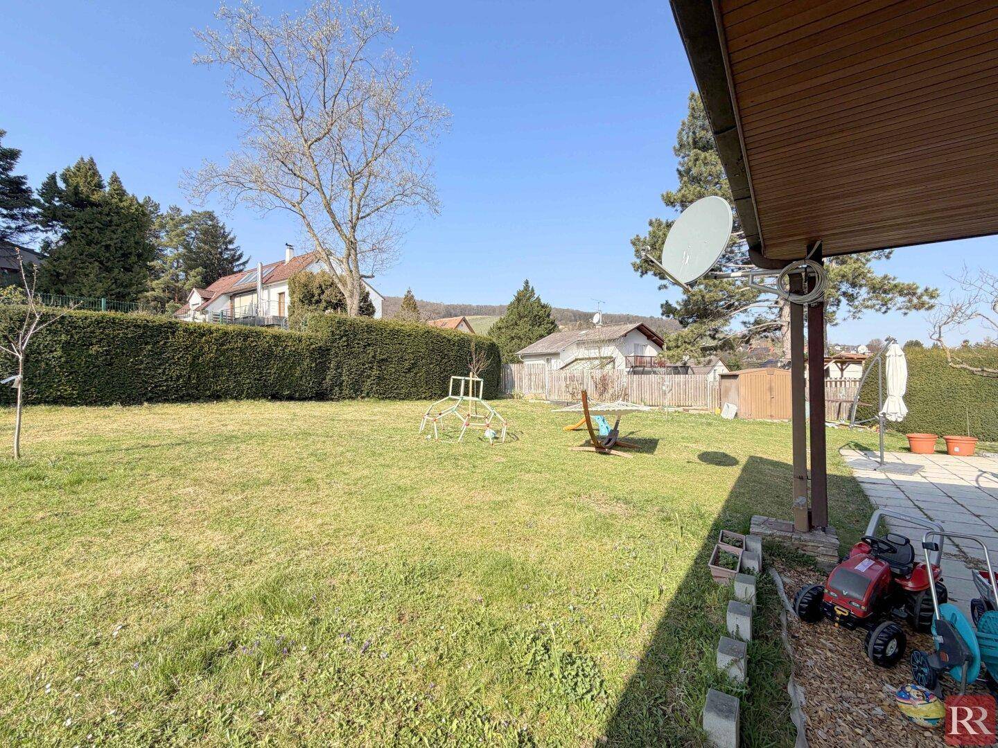 Gartenbereich mit hoher Hecke, Bäumen und Kinderspielgeräten.