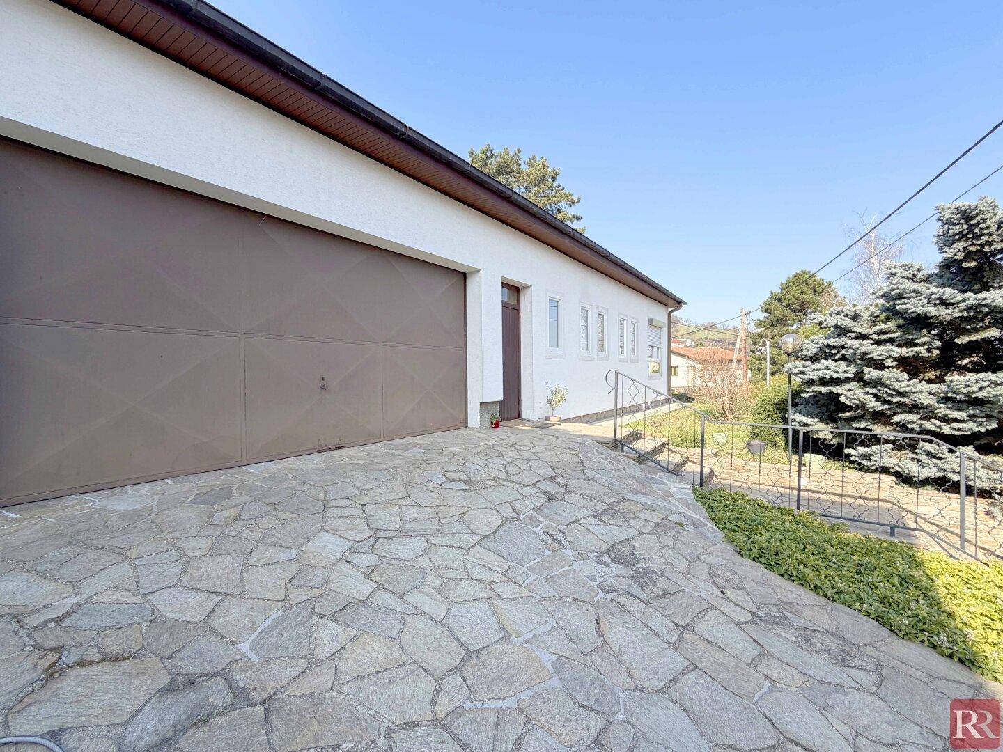 Einfahrt mit Natursteinpflaster und großer Garage.