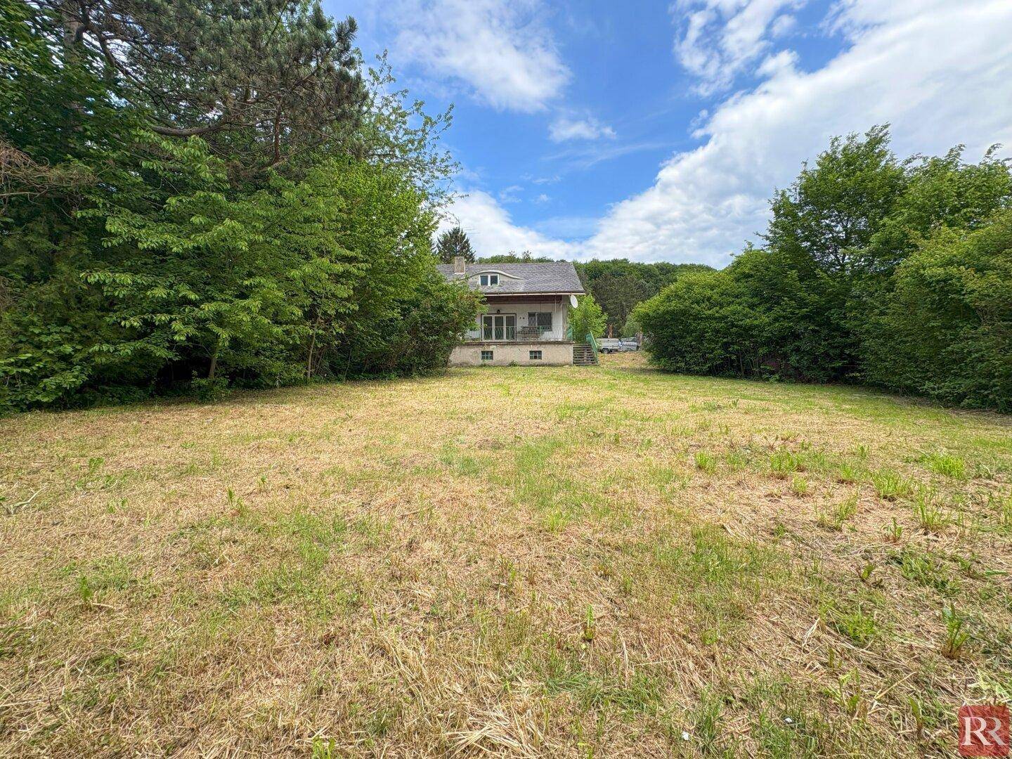 Weitläufiger Gartenbereich mit Blick auf das Einfamilienhaus, umgeben von Bäumen und Natur.