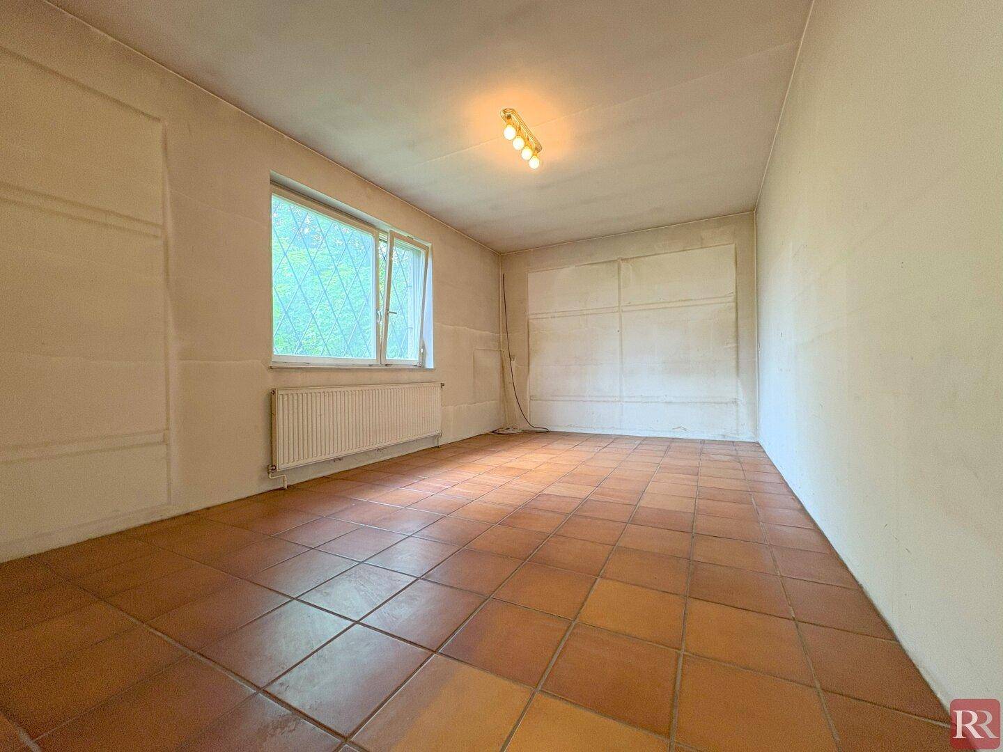 Helles Zimmer mit Terrakottafliesen und Fensterblick ins Grüne.