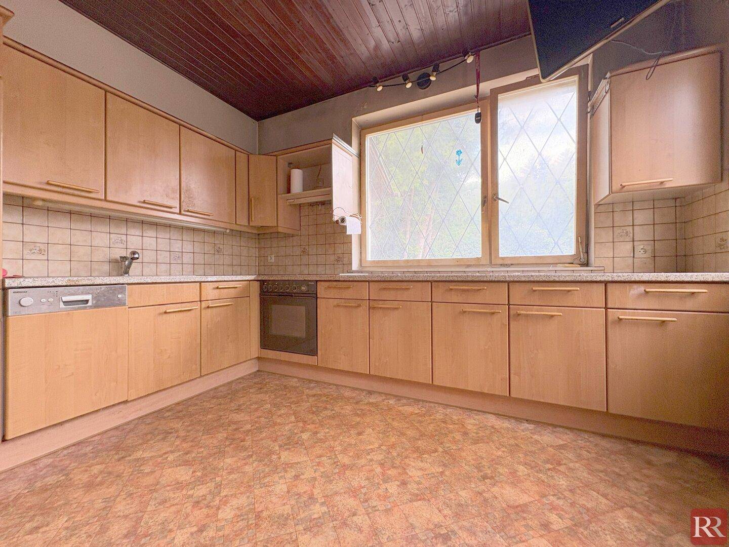 Einbauküche mit Holzschränken, Spülmaschine und Fenster mit Blick ins Grüne.