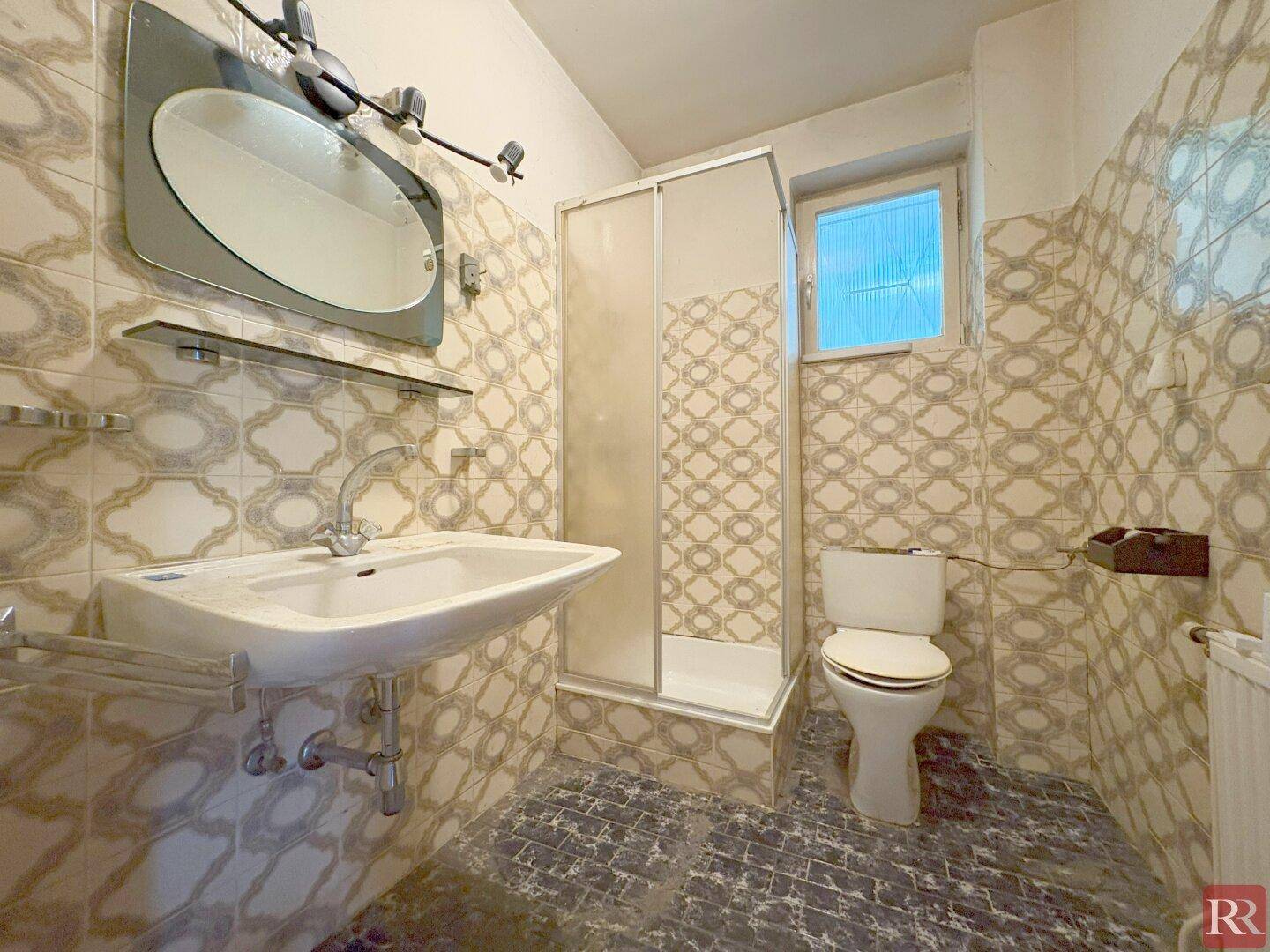 Badezimmer mit Duschkabine, Waschbecken und WC, gefliest in beigen Mustern.