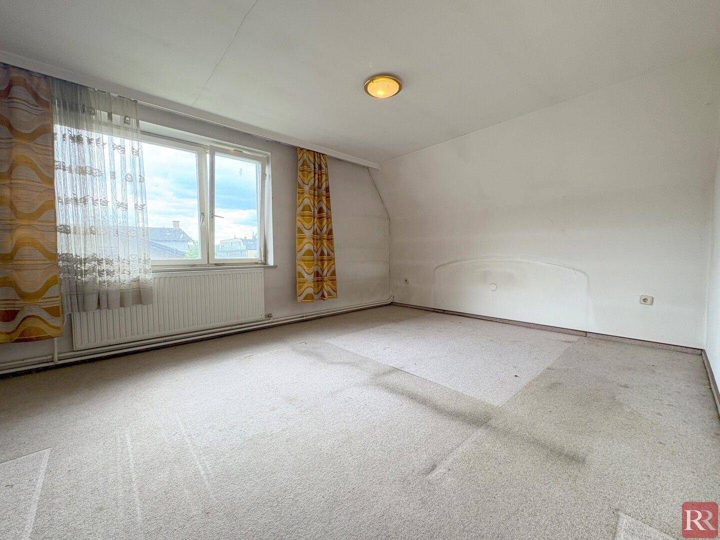 Dachgeschoss-Schlafzimmer mit Teppichboden, Fenster und schrägen Wänden.