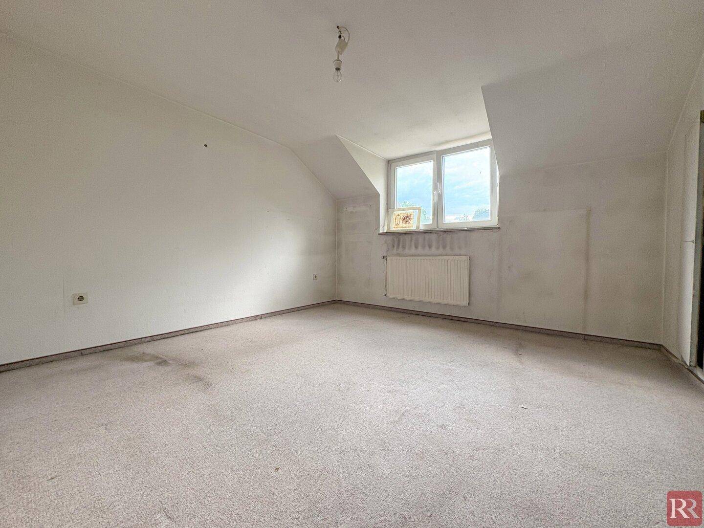 Geräumiges Dachgeschoss-Schlafzimmer mit Teppichboden und Fenster, ideal für Ruhe.