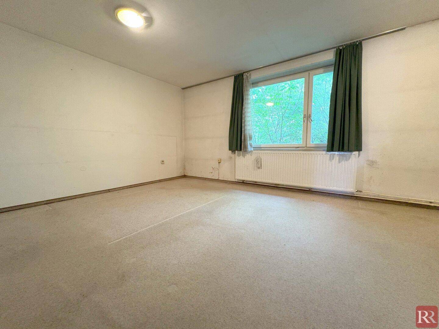 Helles Schlafzimmer mit Teppichboden und Fenster, umgeben von grüner Aussicht.