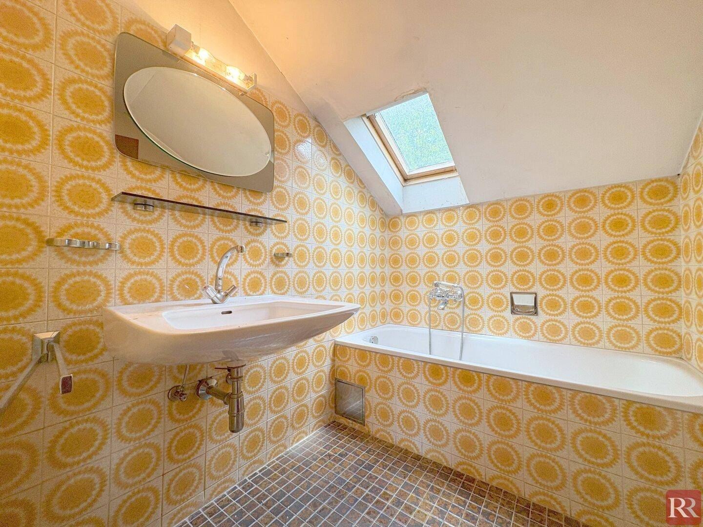 Badezimmer im Dachgeschoss mit gelben Fliesen, Badewanne und Dachfenster.