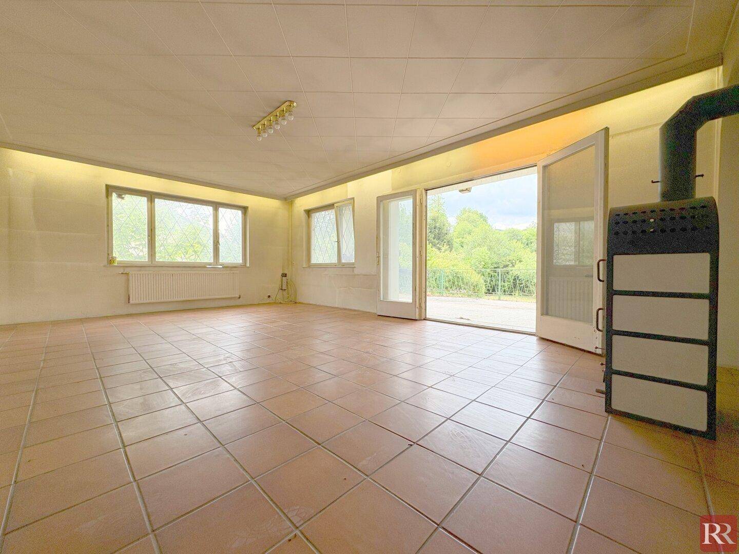 Großes Wohnzimmer mit Terrakottafliesen, Kaminofen und Zugang zur Terrasse.