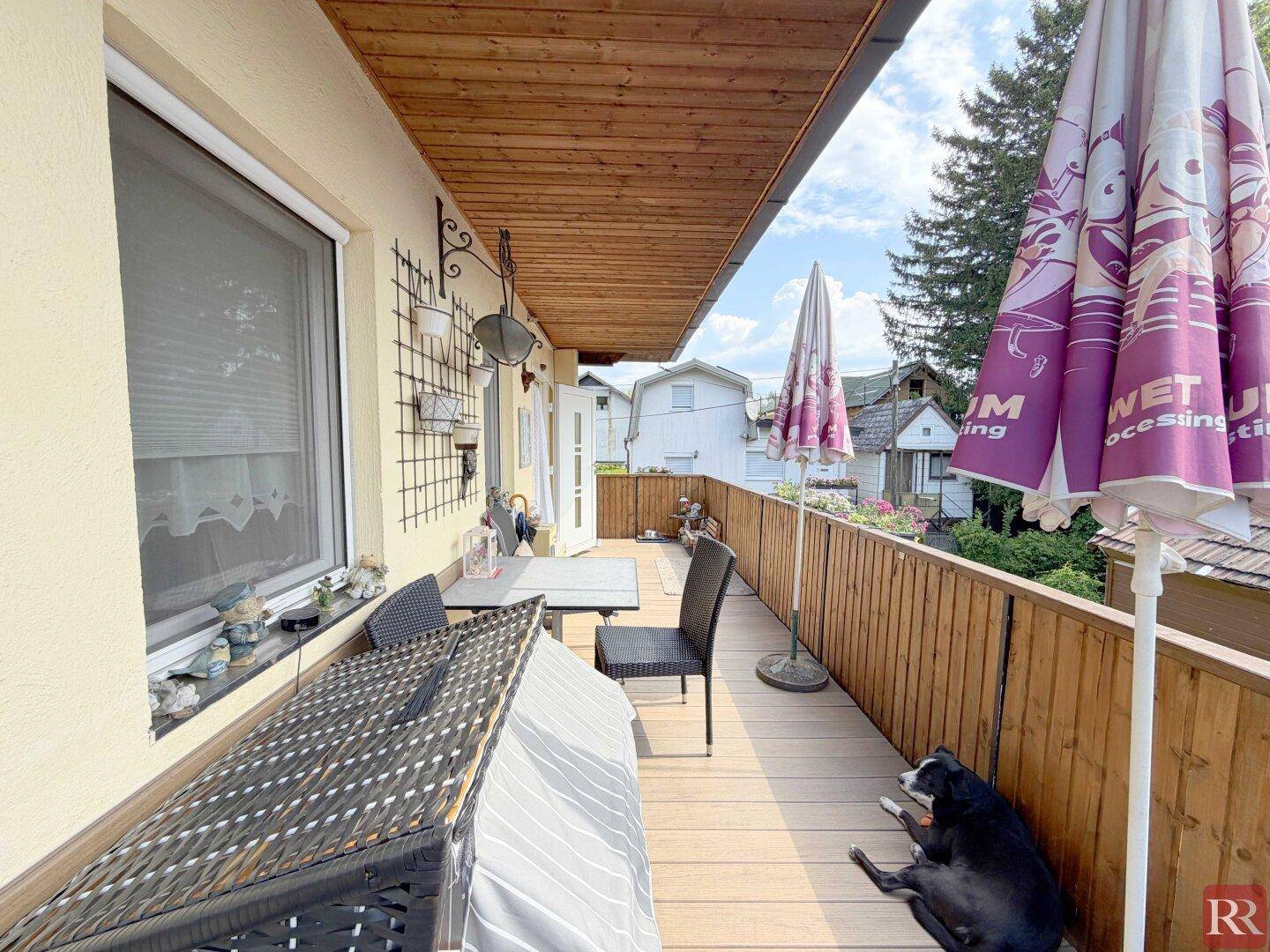 Geräumiger Holzbalkon mit Sitzgelegenheiten und Blick auf die umliegende grüne Umgebung.