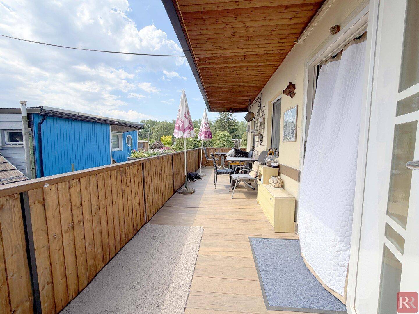 Langer Holzbalkon mit Zugang zum Innenbereich und Blick auf den Garten und die Nachbarschaft.