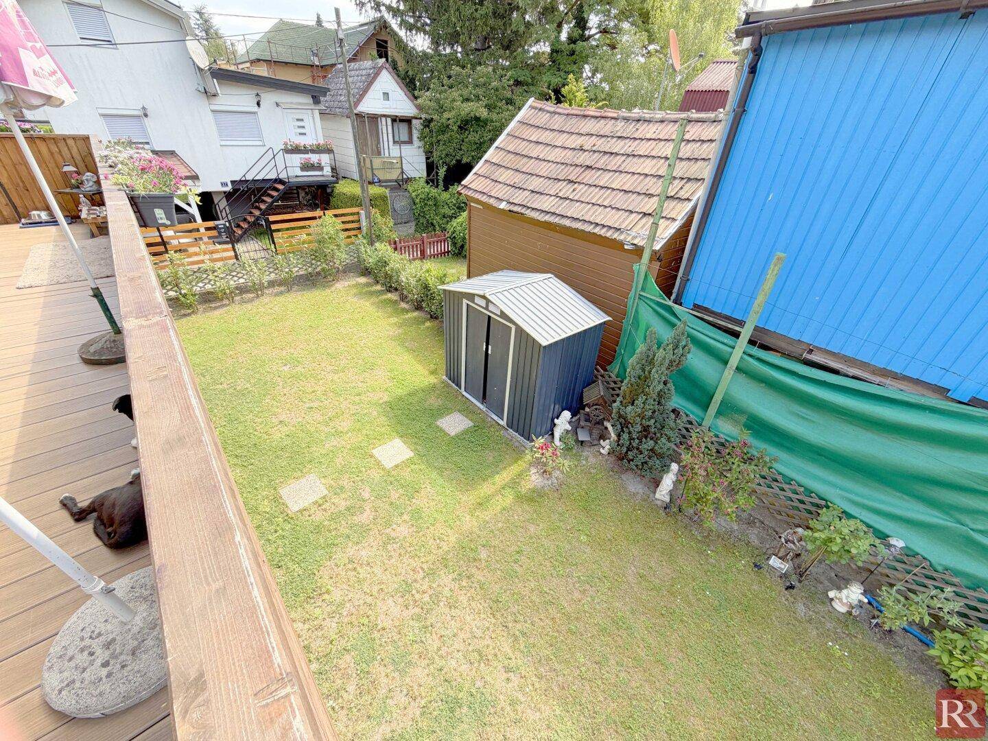 Blick vom Balkon auf den gepflegten Garten mit Rasenfläche und einem kleinen Geräteschuppen.
