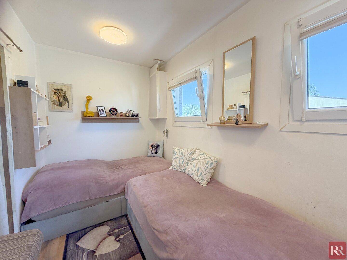 Helles Schlafzimmer mit zwei Einzelbetten, Fenster und einfacher, funktionaler Einrichtung.