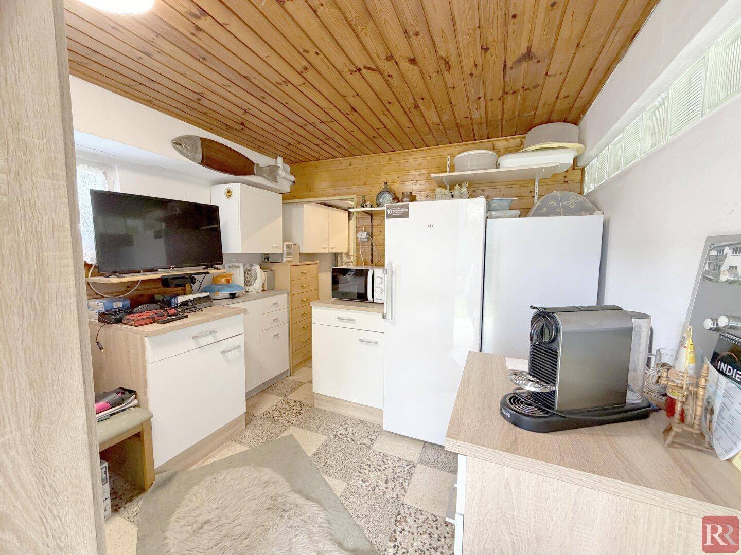Funktionale Küche mit Holzdecke, weißen Schränken und verschiedenen Haushaltsgeräten.