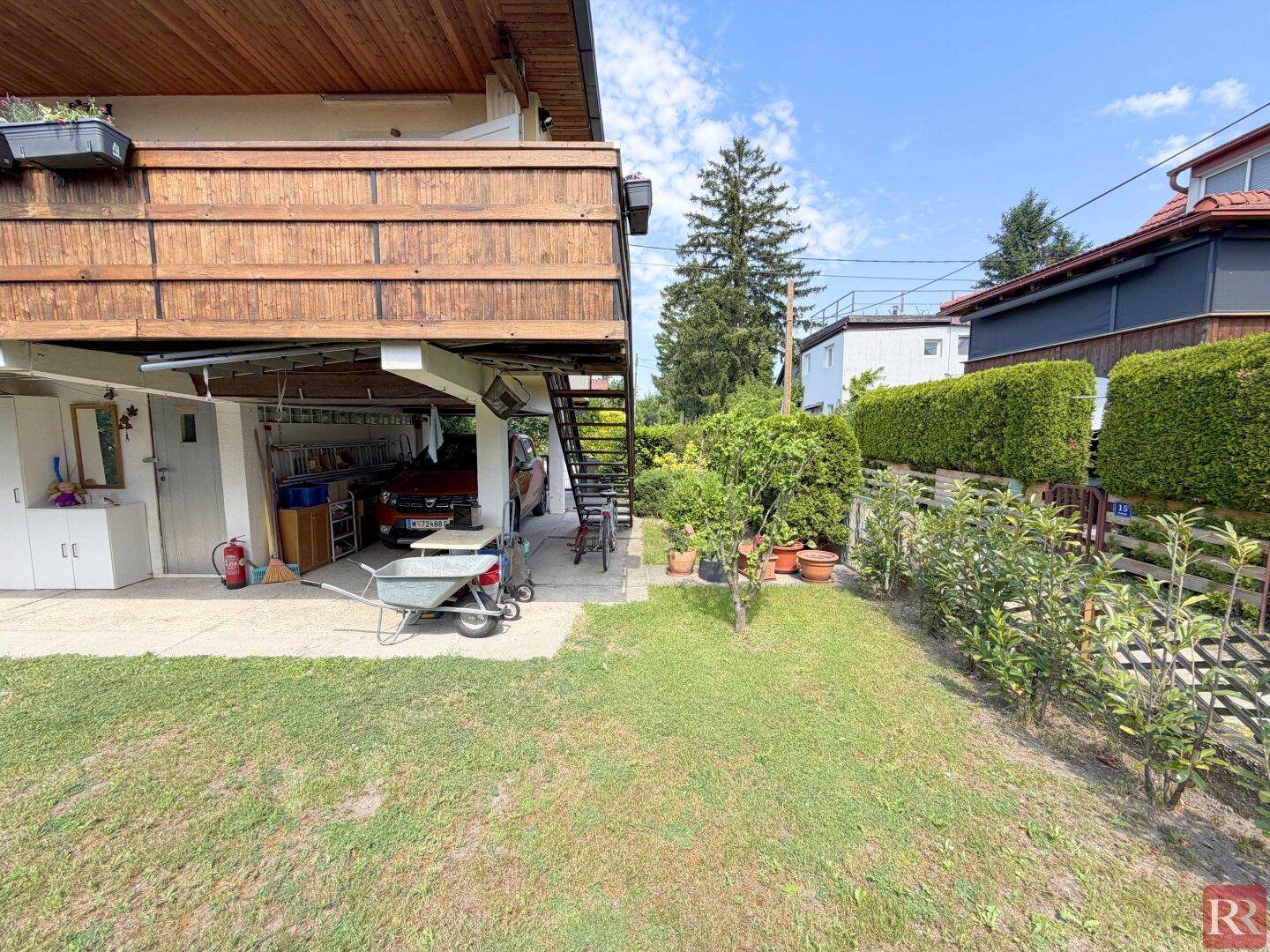 Seitlicher Blick auf das Haus mit Garten, Treppe zum Balkon und überdachtem Bereich.