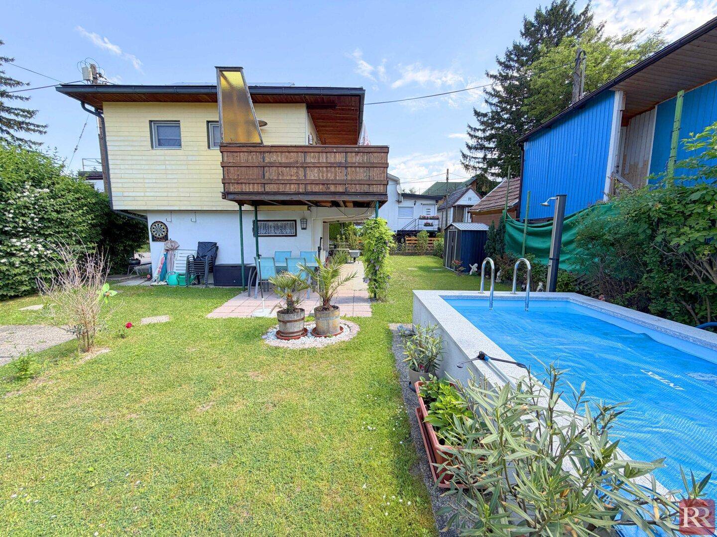 Sonniger Garten mit Rasenfläche, eingelassenem Pool und Terrasse am Haus.