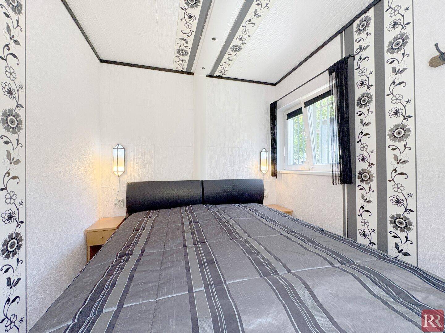 Schlafzimmer mit Doppelbett, gemusterter Tapete und Deckenpaneelen, die dem Raum Charakter verleihen.