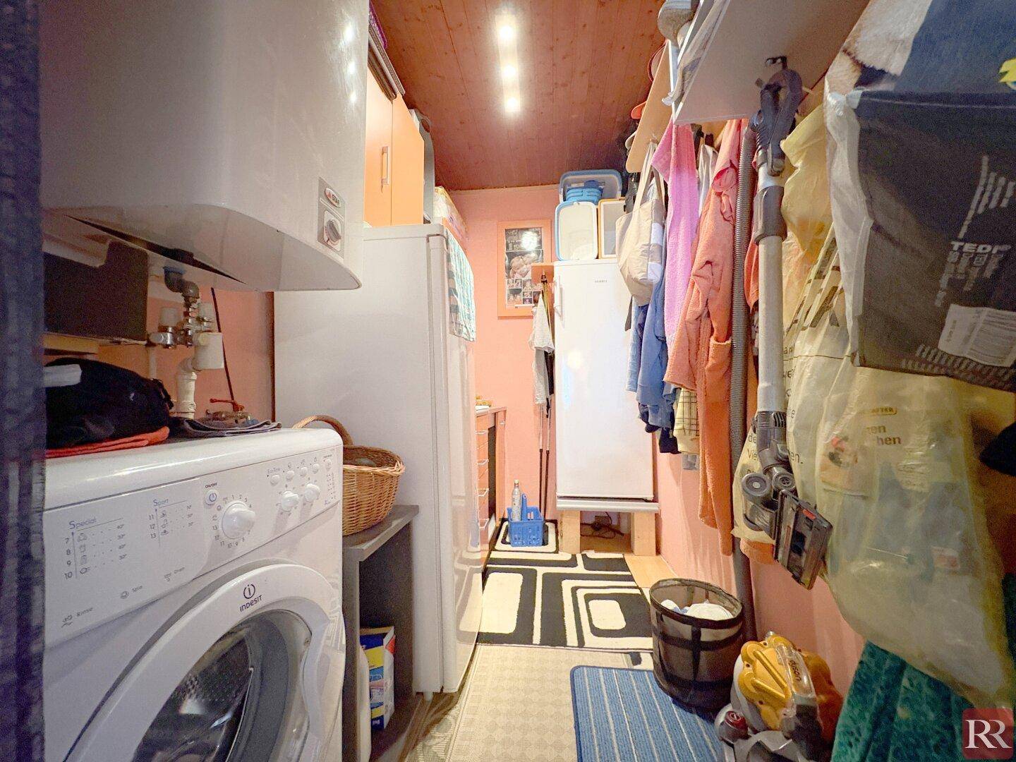 Praktischer Hauswirtschaftsraum mit Waschmaschine, Kühlschrank und Regalen für zusätzlichen Stauraum.