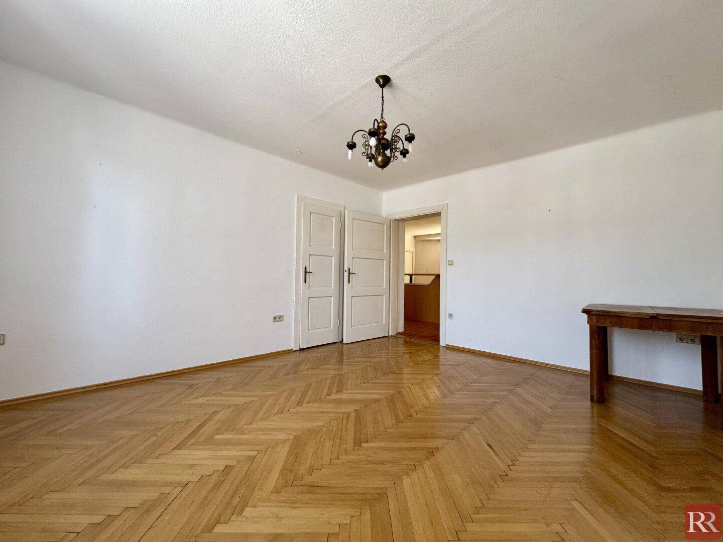 Helles Wohnzimmer mit klassischem Fischgrätparkett und einer Holztür, bereit zur individuellen Gestaltung.