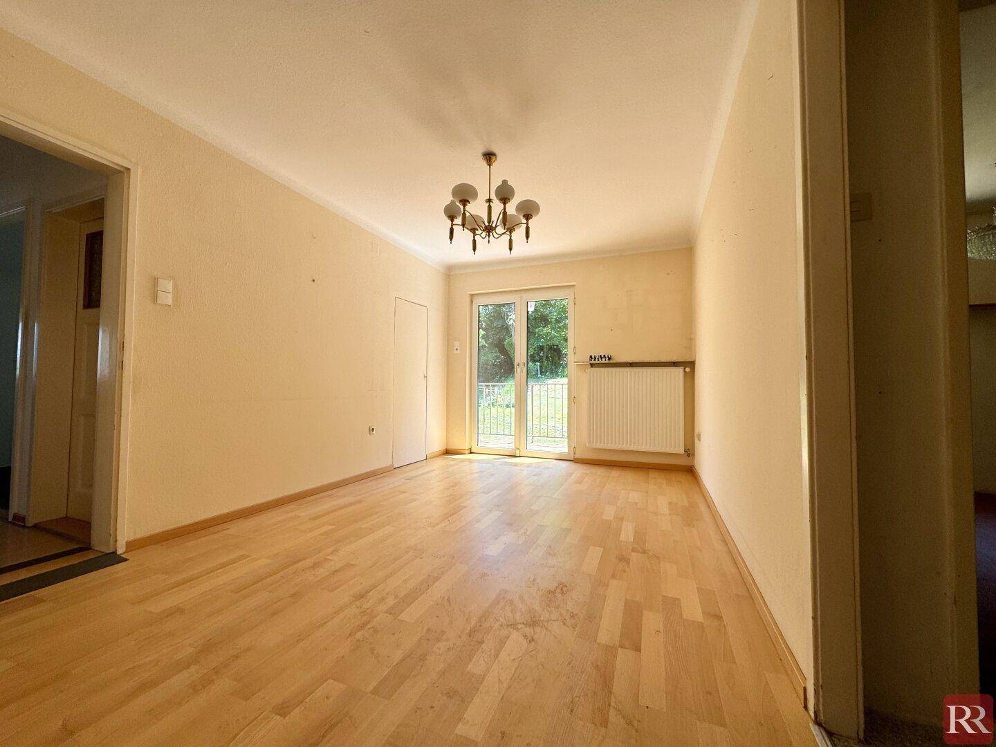 Helles Zimmer mit Holzboden und direktem Zugang zu einem Balkon oder einer Terrasse durch eine Glastür.